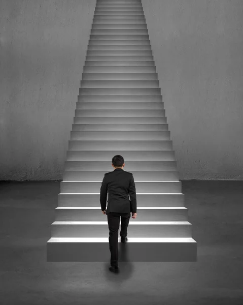 Rear view businessman climbing on stairs with spot lighting — Stock Photo, Image