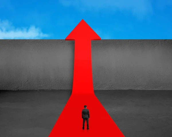 Businessman standing on growing red arrow with wall and sky — Stock Photo, Image