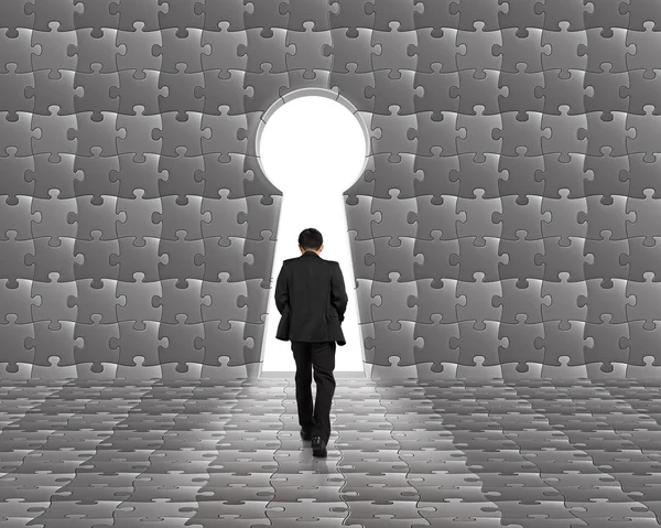 Businessman walking toward key shape door on puzzle wall — Stock Photo, Image