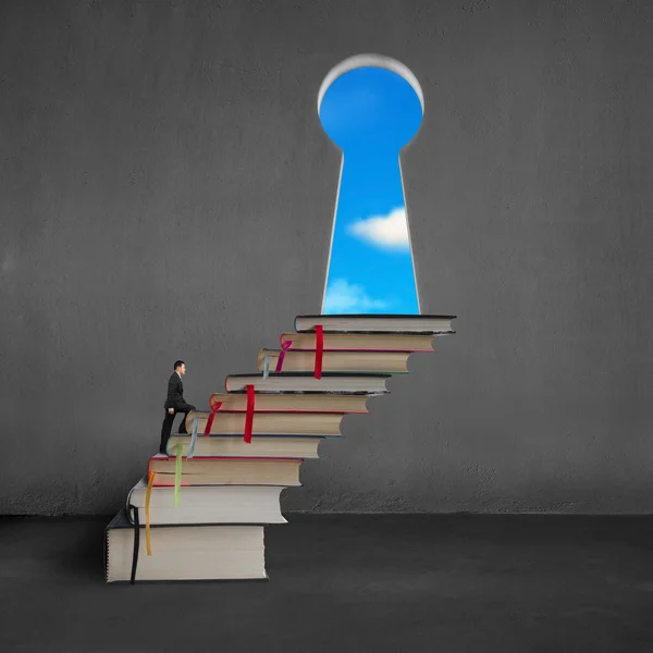 Businessman climbing on stack books to key shape door — Stock Photo, Image