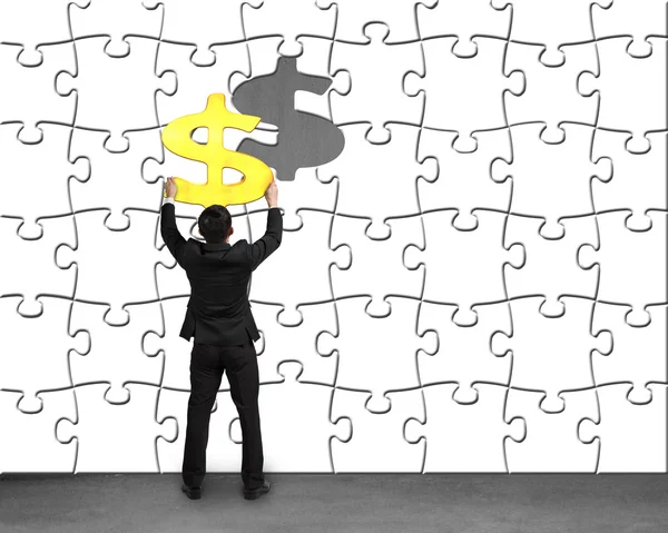 Businessman holding money symbol assembling to puzzles wall — Stock Photo, Image