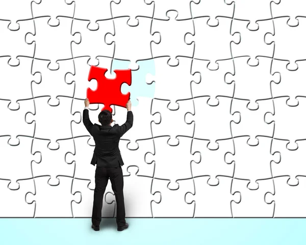 Homme d'affaires assemblant puzzle rouge unique au mur de puzzles blancs — Photo