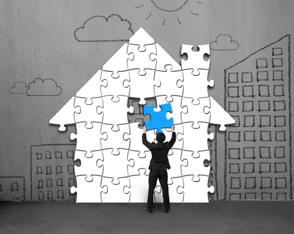 Colocando últimos puzzles azuis em forma de casa na parede — Fotografia de Stock
