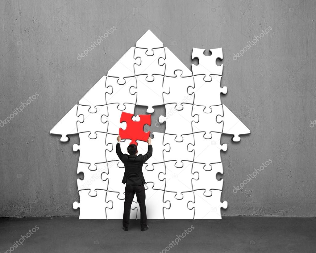 Putting red puzzle into house shape on wall