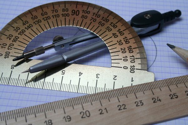 Компасы, карандаш и линейка на квадратной бумаге
