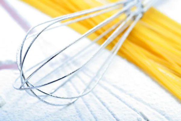 Wire whisk and spaghetti on flour — Stock Photo, Image