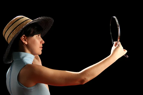 Молодая женщина в соломенной шляпе смотрит в зеркало — стоковое фото