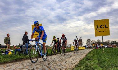 Templeuve, Fransa - 08 Nisan 2018: Paris-Roubaix 2018 sırasında Templeuve geleneksel Vertain yel değirmeni önünde Arnavut kaldırımlı yolda sürme peloton. 