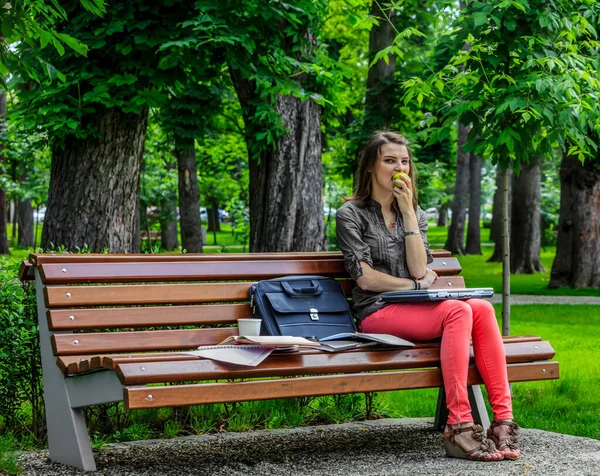 Jovem Mulher Sentada Banco Parque Trabalhando Laptop Enquanto Come Uma — Fotografia de Stock