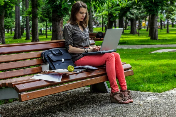 一个年轻的女人在外面的一个公园里的长椅上学习 主要的焦点是被咬的苹果 — 图库照片