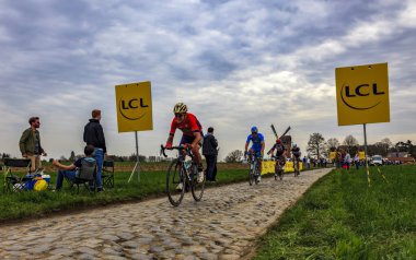 Templeuve, Fransa - 08 Nisan 2018: Paris-Roubaix 2018 sırasında Templeuve geleneksel Vertain yel değirmeni önünde Arnavut kaldırımlı yolda sürme peloton. 