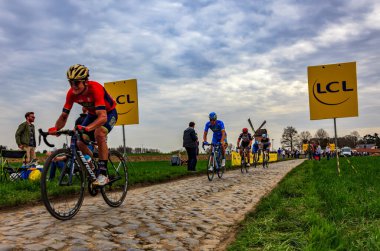 Templeuve, Fransa - 08 Nisan 2018: Paris-Roubaix 2018 sırasında Templeuve geleneksel Vertain yel değirmeni önünde Arnavut kaldırımlı yolda sürme peloton. 