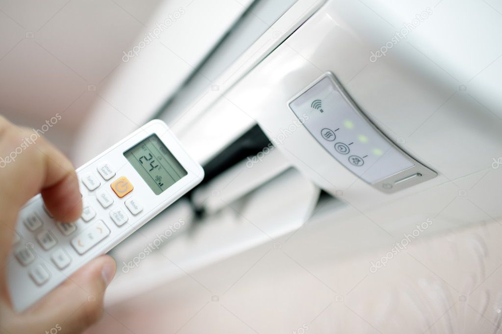 Air conditioner on the wall in the room and hand with the remote control switch to the desired degree