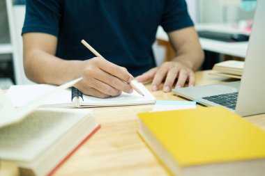 Genç adam evdeki dizüstü bilgisayarın önünde ders çalışıyor.