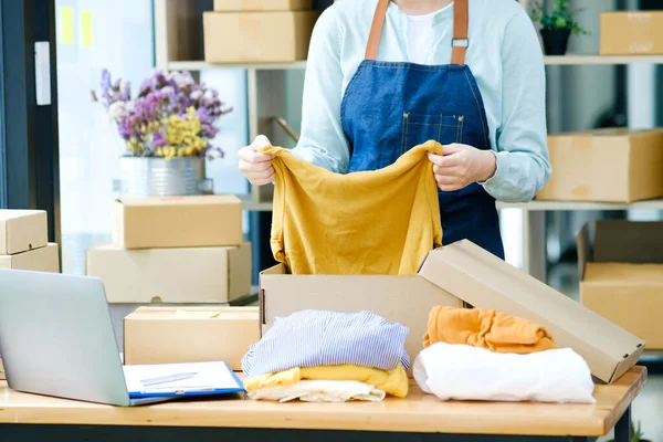 Asiático feminino loja de roupas proprietário dobrar uma t-shirt e embalagem em uma caixa de papelão pacote.. — Fotografia de Stock