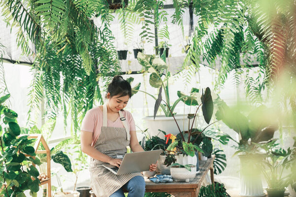 Beautiful female smiling works at garden centre retail store. Taking orders over the phone. She working at table and in background is a shop with lots of plant.