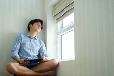 Asyalı yakışıklı iş adamı, pencereden dışarı bakıyor ve tableti elinde tutuyor..