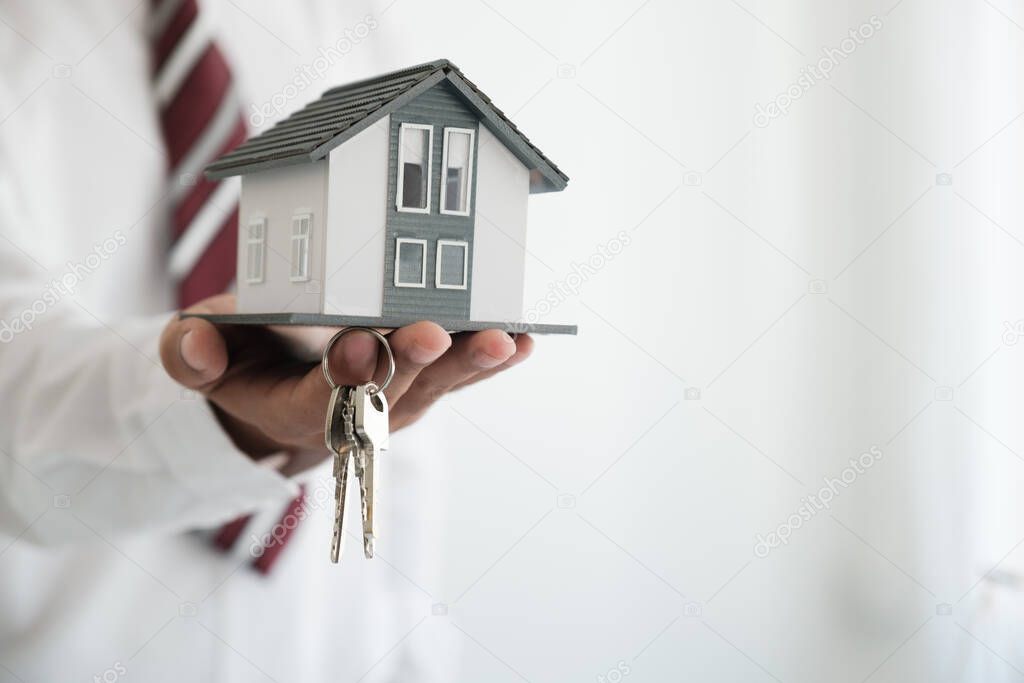 Businessman holding a house model and House Keys.