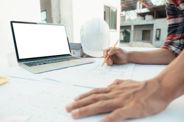 Genç adam cetvel, kalem, mezura, mimar şapkası ve diğer ekipmanlarla bir bina ya da mimari tasarım yapıyordu..