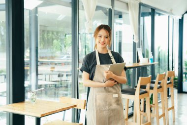 Genç işletme sahibi gülümseyerek ayakta duruyor ve kahve dükkanında çalışıyor sipariş alıyor. Küçük iş adamı konsepti.