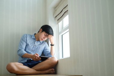 Genç Asyalı yakışıklı işadamı pencereden dışarı bakıyor ve tableti elinde tutuyor..