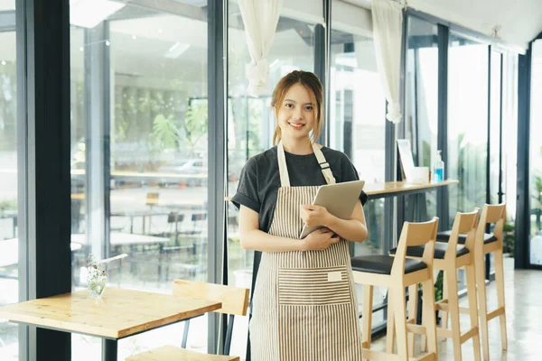 Genç işletme sahibi gülümseyerek ayakta duruyor ve kahve dükkanında çalışıyor sipariş alıyor. Küçük iş adamı konsepti.