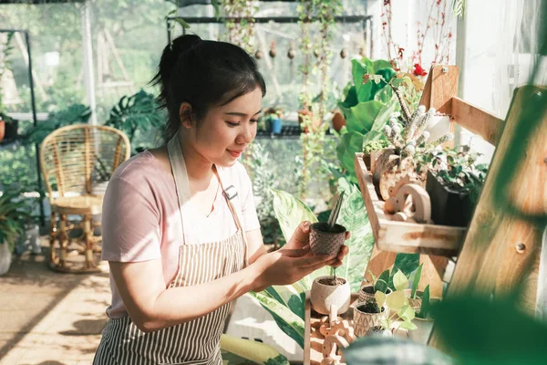 Portrait of a smiling young woman holding a plant in a small gardening shop.