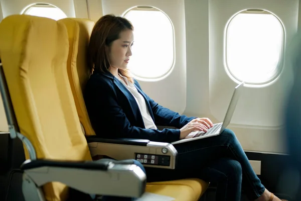 Young businesswoman In a plane using on laptop computer during In a plane flight, travel concept.