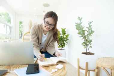 Bilgisayar ve mobil cihaz kullanan genç kolaj öğrencisi, sandalyede oturan bir kitap okuyor, çevrimiçi eğitim veya kendi kendine öğrenim kavramı..