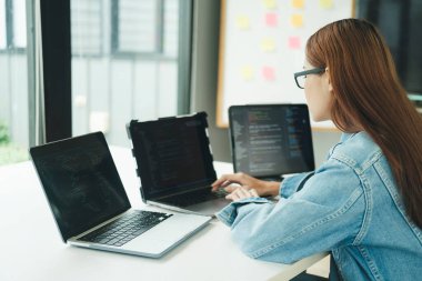 Genç programcı ya da bilişim uzmanı yaptığı işten memnun. Ofisinde çalışırken dizüstü bilgisayarda çalışan mutlu genç bir kadın..