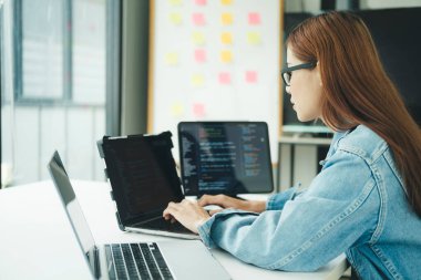 Genç programcı ya da bilişim uzmanı yaptığı işten memnun. Ofisinde çalışırken dizüstü bilgisayarda çalışan mutlu genç bir kadın..