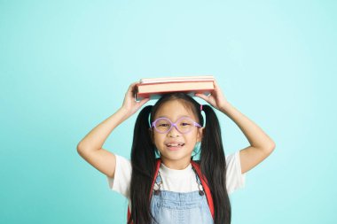 Kid students going to school, girl funny smiling, kid students girl with glasses hold books on her head, blue studio background, school concept.