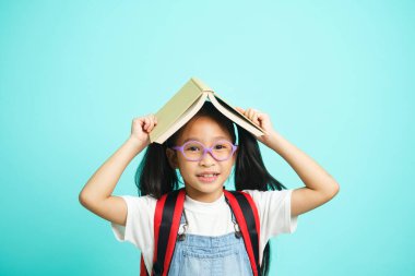 Kid students going to school, girl funny smiling, kid students girl with glasses hold books on her head, blue studio background, school concept.