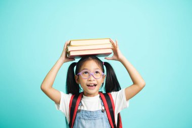 Kid students going to school, girl funny smiling, kid students girl with glasses hold books on her head blue studio background, school concept.