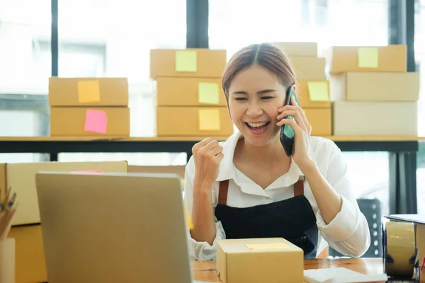 Young Asian businesswoman startup entrepreneur SME owner picking up a yellow shirt before packing it in an inner box with a customer. Online Business Ideas and Freelance.