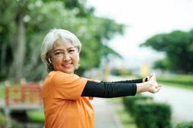 Athletic Senior woman jogger warming up by stretching arms and upper body before running in park.