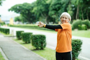Athletic Senior woman jogger warming up by stretching arms and upper body before running in park.