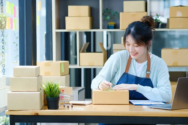Online small business owner writing address on parcel box for delivery to customer, shipping and logistic, merchant online and seller, business owner or SME, online shopping.