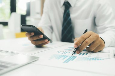 Genç Asyalı girişimci akıllı telefonu kullanarak çevrimiçi pazarlama bilgilerini analiz ediyor.