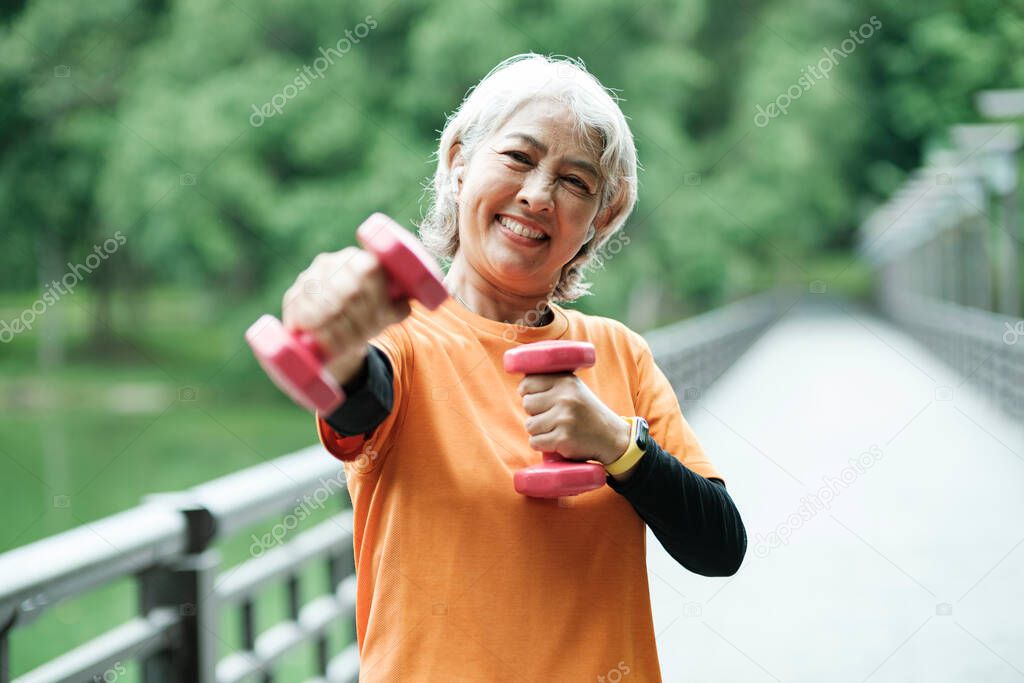 Athletic Senior woman lifts dumbbells while doing fitness before running in park, health concept.