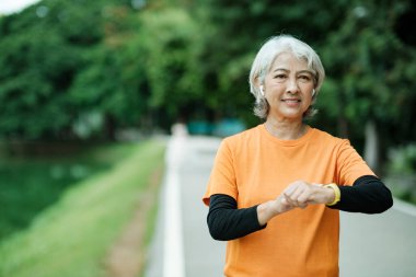 Happy athletic Senior woman checking her smartwatch in the park, Concept of a healthy lifestyle on retirement. health concept.
