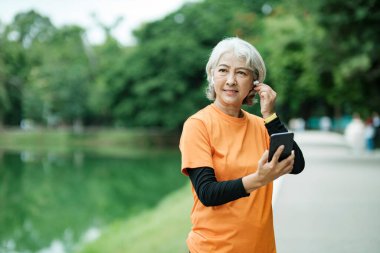 Happy athletic Senior woman listening to music on mobile phone and checking her smartwatch in the park, Concept of a healthy lifestyle on retirement. health concept.