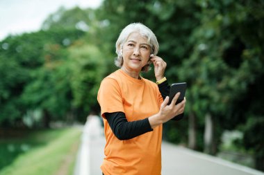Happy athletic Senior woman listening to music on mobile phone and checking her smartwatch in the park, Concept of a healthy lifestyle on retirement. health concept.
