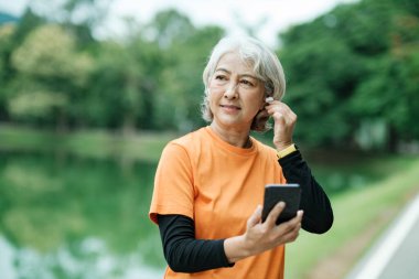 Happy athletic Senior woman listening to music on mobile phone and checking her smartwatch in the park, Concept of a healthy lifestyle on retirement. health concept.