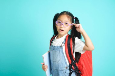 Smiling little girl in glasses pointing finger upward going to school, her face with her index finger pointing up and smiling, after coming up with an idea for her school assignment, school concept
