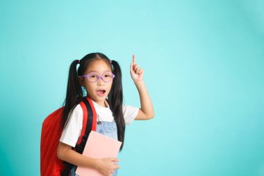 Smiling little girl in glasses pointing finger upward going to school, school concept. standing on a blue background.