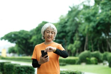 Happy athletic Senior woman checking her smartwatch in the park, Concept of a healthy lifestyle on retirement. health concept.