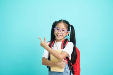 Smiling little girl in glasses pointing finger upward going to school, school concept. standing on a blue background.
