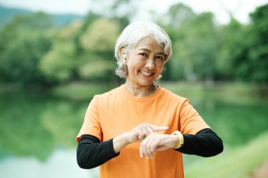 Happy athletic Senior woman checking her smartwatch in the park, Concept of a healthy lifestyle on retirement. health concept.