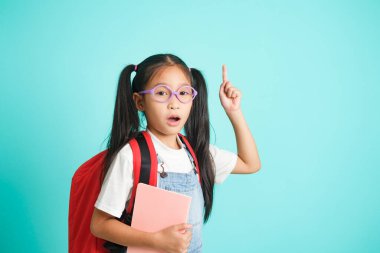 Smiling little girl in glasses pointing finger upward going to school, school concept. standing on a blue background.